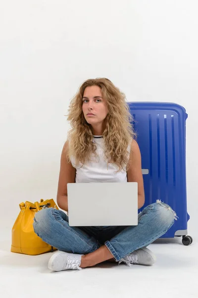 Beautiful young woman with laptop and suitcase on white background