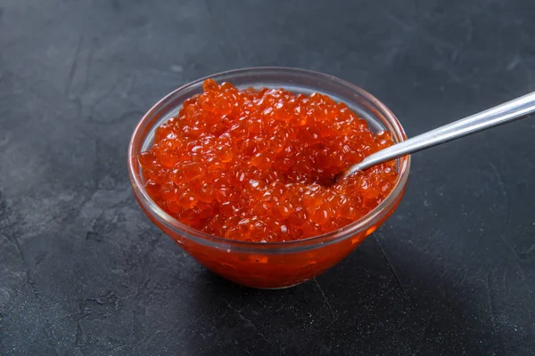 Red caviar in glass jar with silver spoon on the dark rustic background