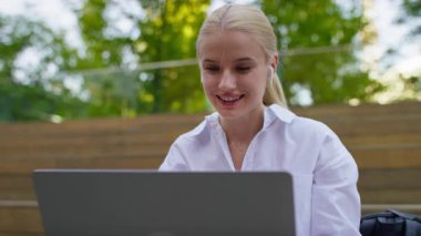 Kulaklık takan neşeli bir kadın güneşli, yeşil bir ortamda otururken laptopunda çalışmaktan ya da gezinmekten hoşlanır..