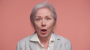Çizgili ceketli yaşlı kadın şaşırmış ve sıkıntılı görünüyor. Büyük gözleri ve ağzı açık, ani kötü haberlere tepki veriyor..