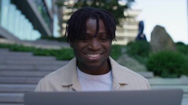 Dışarıda mutlu bir gencin yakın plan fotoğrafı. Alnında gülümseyerek dizüstü bilgisayarında olumlu haberler okuyor..