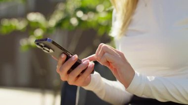 Açık havada kadın el ele tutuşurken ve modern akıllı telefon kullanırken, muhtemelen doğal ışık altında mesajlaşırken ya da gezinirken..