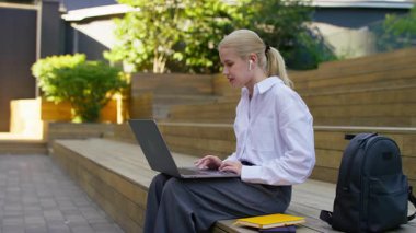 Dışarıda dizüstü bilgisayarla oturan genç bir kadın, muhtemelen kötü akademik ya da kişisel haberler aldıktan sonra hayal kırıklığı ya da üzüntü gösteriyor..