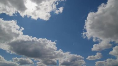 Dinamik gökyüzü görünümü tüylü beyaz bulutların parlak mavi bir arkaplanda sürüklendiğini gösteriyor, hızlandırılmış veya hava durumu görselleri için ideal.