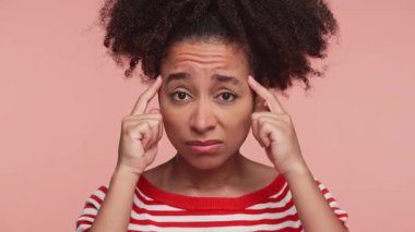 Kırmızı çizgili gömlekli genç bir kadın şakaklarına işaret ediyor. Pembe arka planda hayal kırıklığı, stres ya da konsantrasyon belirtileri gösteriyor..