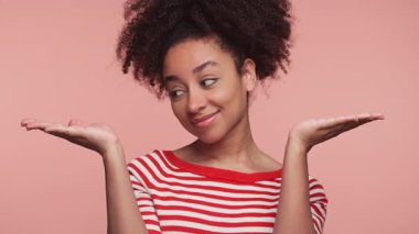 Kırmızı çizgili gömlekli genç kadın iki elini havaya kaldırdı. Pembe arka plandaki seçenekleri karşılaştırıyor ya da tartıyor gibiydi..