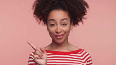 Kırmızı çizgili tişörtlü genç bir kadın parmağını yukarı kaldırarak gülümsüyor pembe bir arka plana karşı şakacı bir uyarı hareketi yapıyor..