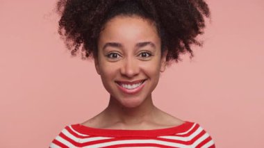 Kırmızı çizgili tişörtlü neşeli genç bir kadın. Gülümsüyor ve kafasını pembe stüdyo geçmişine doğru sallıyor..