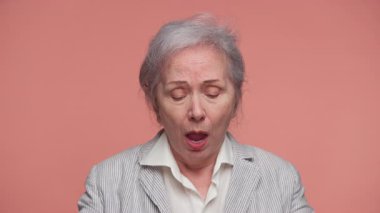 Yaşlı kadın gözlerini kapatmış ve ellerini başının üstüne koymuştu. Pembe arka planda stres, baş ağrısı ya da duygusal bunalımı ifade ediyordu..