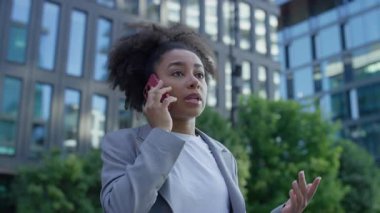 Genç, profesyonel bir kadın akıllı telefonuyla konuşurken, modern bir şehir iş bölgesinde aciliyet ve endişeyi dile getiriyor..