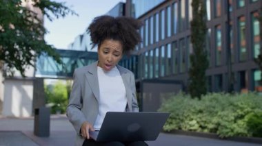Sorunlu genç profesyonel kadın dışarıda dizüstü bilgisayarla oturuyor. Beklenmedik işten çıkarma haberleri aldıktan sonra kafasını inançsızlıkla tutuyor..