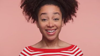 Kırmızı ve beyaz çizgili süveter giyen mutlu genç bir kadın pembe arka planda parlak bir gülümsemeyle başını sallıyor..