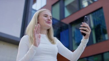 Modern bir ofis binasının önünde elinde akıllı telefon tutan ve sohbet eden gülümseyen bir öğrenci..