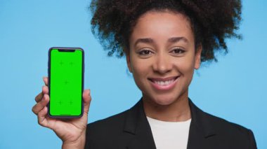 blazer ceketli mutlu genç kadın akıllı telefonu parlak mavi arka plana karşı yeşil ekran görüntüsüyle sunar. Uygulama tasarımı için ideal..