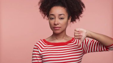 Kırmızı çizgili tişörtlü genç bir kadın el hareketi yaparak pembe arka plana karşı hoşnutsuzluğunu ya da anlaşmazlığını dile getiriyor..