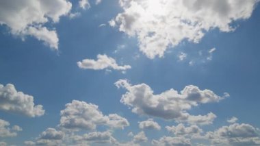 Pofuduk beyaz bulutların parlak mavi gökyüzünde güneş ışığıyla sürüklenip dinamik ve huzurlu bir manzara yarattığını gösteren güzel bir zaman atlaması sahnesi..