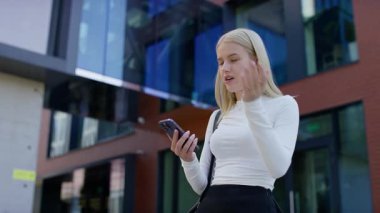 Endişeli genç kadın akıllı telefonu tutuyor ve dışarıda endişeli bir ifadeyle yüzüne dokunuyor.