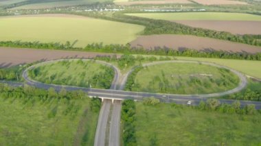 Güneşli bir yaz gününde yeşil tarlaların arasından geçen karayolu üzerindeki hava manzarası. Çayır ve kırsal alan arasında asfalt çevre yolu olan 4K manzara görüntüsü. Drone kırsal kesimin videosunu çekiyor.