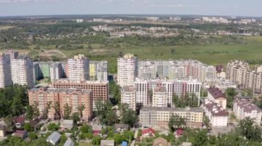 Yazın güneşli bir günde mavi silueti olan yeşil şehir manzarasının hava görüntüsü. Şehirdeki ağaçlar arasındaki binaların 4K videosu. Şehir manzarasının güzel manzarası.