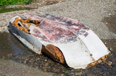 Hasarlı gövdenin kıyısında terk edilmiş ters dönmüş bir tekne var..