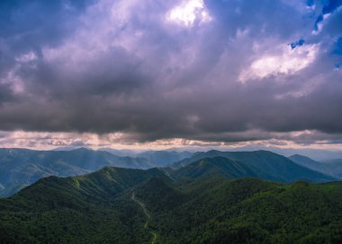 Hava görüntüsü. Kasvetli bulutlu gökyüzünün altındaki dağlar. Dağın içinden geçen yol..
