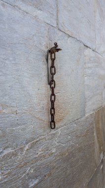 Paslı bir zincir parçası taş duvarda asılı..