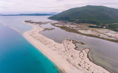 Durgun su, turkuaz denizden kumlu bir tükürükle ayrılır..