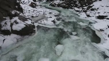 Rusya 'nın Kafkasya dağlarında karla kaplı bir vadinin dibindeki hızlı bir dağ deresinin turkuaz suları..