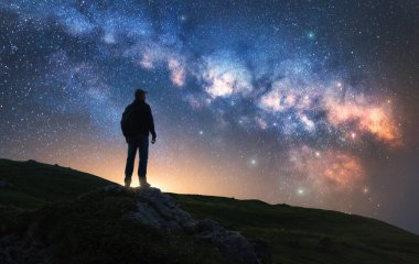 Parlayan Samanyolu ve yıldızlı gecede dağın zirvesinde bir adam. Tepede parlak yıldızlı bir adamın silueti. Galaksi. Samanyolu ile uzay manzarası. Gece manzarası. Seyahat geçmişi. Kavram