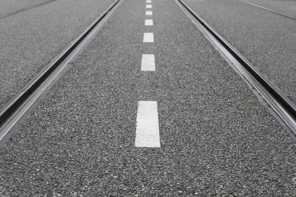 Пустая улица с белой пунктирной линией и параллельными трамвайными путями
