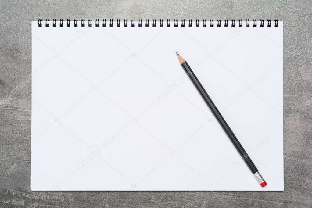 Blank page of a sketchbook with a black pencil on a grunge gray surface