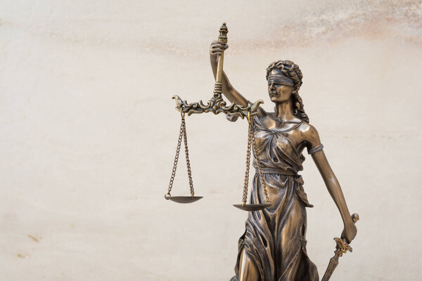 The statue of justice Themis or Justitia, the blindfolded goddess of justice against marble wall background, as a legal concept