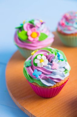 Renkli çiçekler ve kelebekler ahşap yuvarlak masa üzerinde üç top kek krem renkli top ile süslenmiş. Anneler günü için bahar pasta