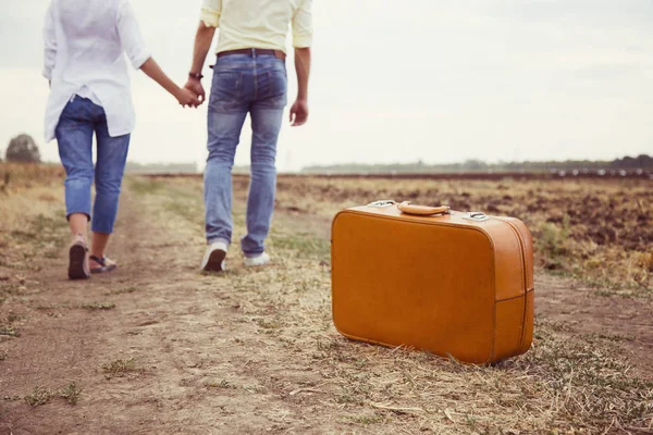 年轻美丽的情侣走在乡村道路上牵手 在浪漫的旅行与棕色手提箱 夏日之旅 — 图库照片