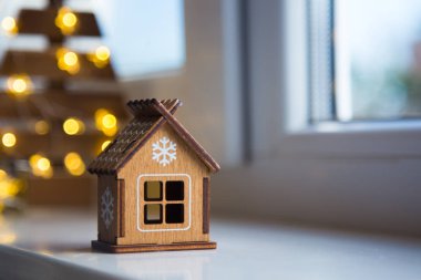 Gün ışığı ve sıcak garland bokeh arka plan üzerinde penceresinde yakınındaki beyaz kar tanesi ile ahşap oyuncak evi. Noel afiş.