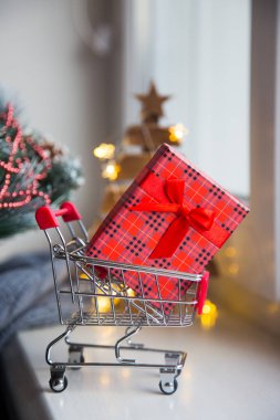 Sıcak garland ışıkları ile küçük süpermarket arabası bokeh arka plan üzerinde kırmızı hediye kutusunda. Noel alışveriş kavramı.
