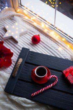Kırmızı fincan espresso kahve karamel kamışı Noel dekorasyon ve çelenk ışık ile karanlık ahşap tepsi ile. Yeni yıl kahvaltı ile Led yıldızı parlayan Amaryllis, hediye kutusu,.