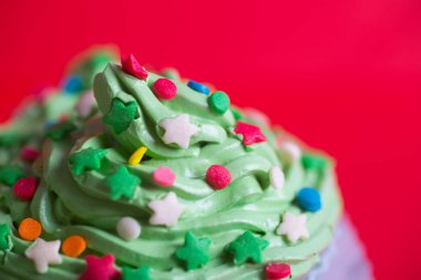 Closeup yılbaşı cupcake krem yeşil ile üst renkli yıldız ve kırmızı zemin üzerine sprinkles. Tatlı Noel ağacı şeklinde