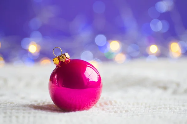 深红色圣诞球在白色针织面料在紫色背景与温暖的 Bokeh 新年贺卡 圣诞装饰 — 图库照片