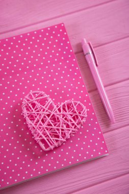 Kalem ahşap pembe tablo ile pembe hasır kalp üstünde lekeli kadın defter. Romantik kart kadınlar için. Sevgililer günü natürmort.