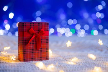 Kırmızı hediye kutusu ile sıcak çelenk ışık ve örme beyaz kumaş üzerine mavi bokeh çevrili. Noel hediyesi. Yeni yıl kartı kopya alanı ile.