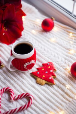 Örme rahat fincan çay ve Noel gingerbread kış dekorasyonu ile çevrili beyaz örme şal üzerinde. Nergis zambağı, Noel topları ve gün ışığından yararlanma penceresinde yakınındaki hediye kutusu. Yeni yıl tatil kompozisyon.