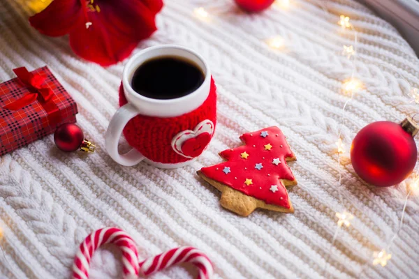 Örme rahat fincan çay ve Noel gingerbread kış dekorasyonu ile çevrili beyaz örme şal üzerinde. Nergis zambağı, Noel topları ve gün ışığından yararlanma penceresinde yakınındaki hediye kutusu. Yeni yıl tatil kompozisyon.