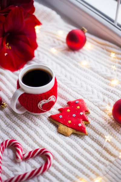 Örme rahat fincan çay ve Noel gingerbread kış dekorasyonu ile çevrili beyaz örme şal üzerinde. Nergis zambağı, Noel topları ve gün ışığından yararlanma penceresinde yakınındaki hediye kutusu. Yeni yıl tatil kompozisyon.