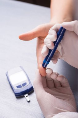 Doktorun elinde şırınga kalem kullanarak hastanın kan şekeri düzeyini kontrol tıbbi lateks eldiven. Şeker Ölçüm masanın üzerinde. Yordam glucosometry için.