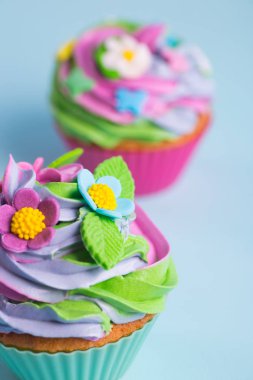 Renkli çiçek ve yaprakları mavi zemin üzerine closeup iki top kek krem renkli üst süslenmiş.