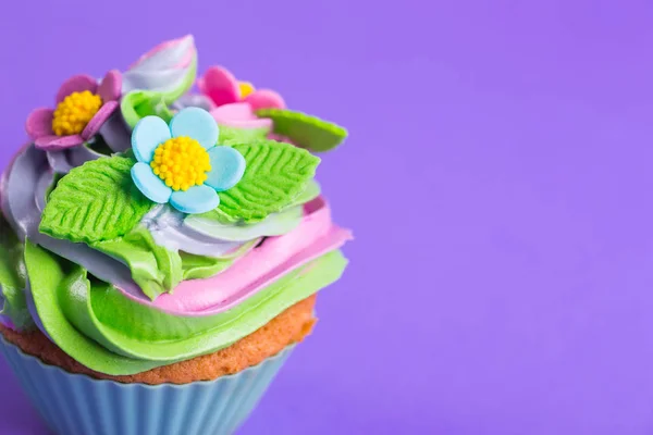 Closeup cupcake cremoso multicolorido top decorado com flores coloridas e folhas no fundo roxo — Fotografia de Stock