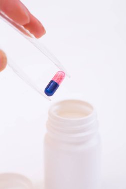 Plastik cımbız elinde iki renkli hap açık plastik kavanozun içine koyarak arka plan beyaz. İş araştırma izole kavramı.