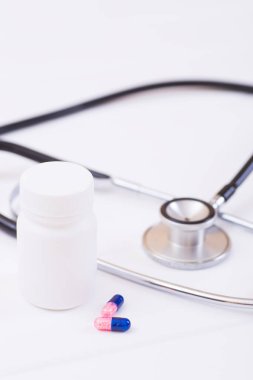 Closeup plastik kavanoz, iki kapsül ve beyaz arka plan üzerinde stetoskop. İç hastalıkları tedavide ilaç tedavisi kavramı.