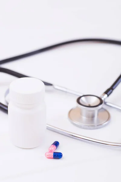 Closeup plastic jar, two capsules and stethoscope on white background. Concept of drug treatment of internal diseases in therapy.